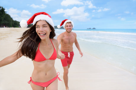 Couple on beach holding hands with santa hats 